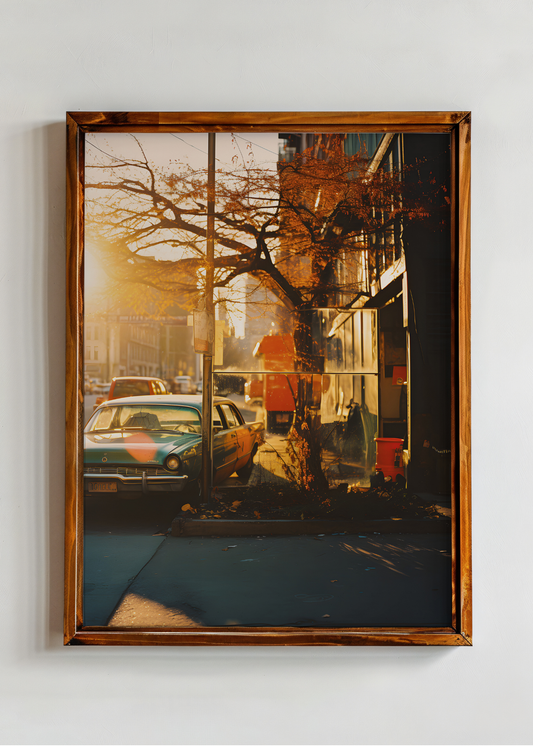 Framed artwork of a city street scene with cars and a tree, on a white wall.