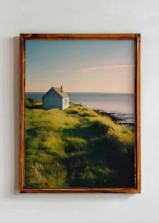 Framed artwork of a coastal scene with a house on a grassy hill.