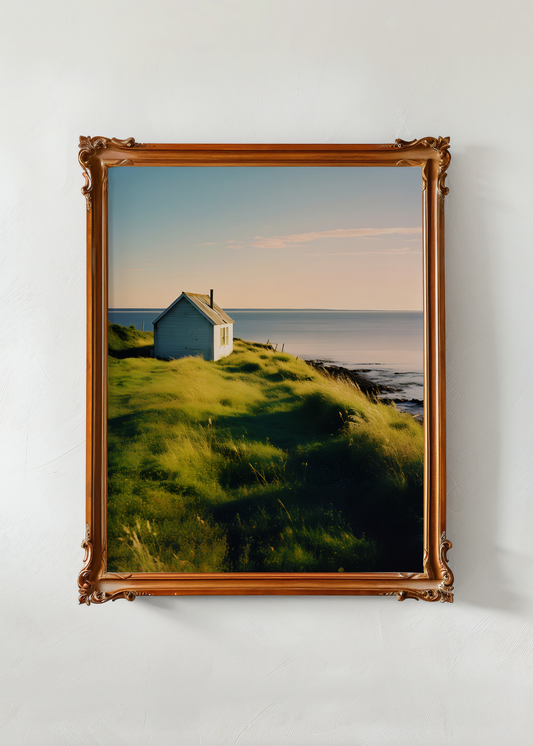 Framed photograph of a coastal scene with a house on a grassy hill.