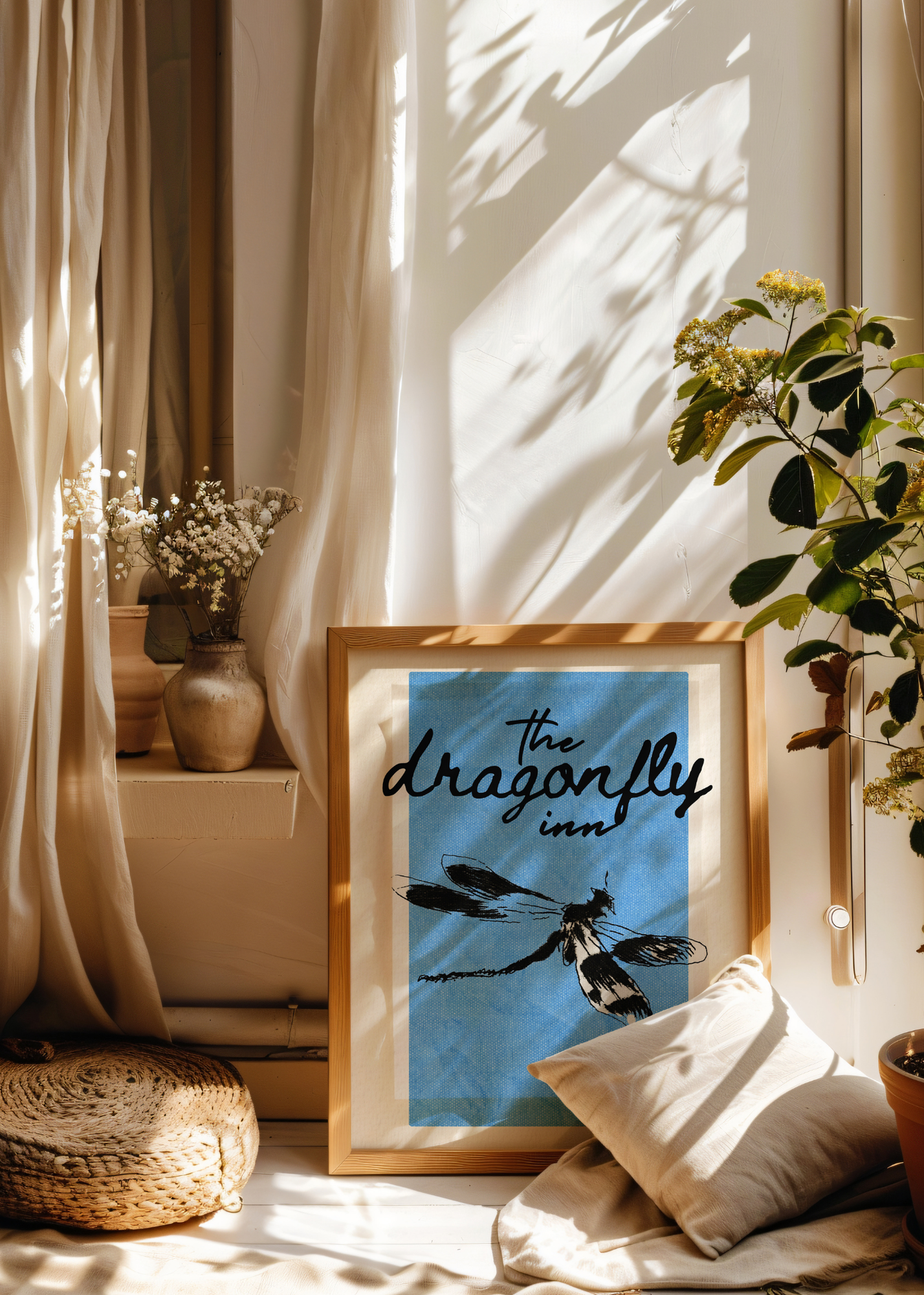 Framed artwork with 'the dragonfly inn' text in a cozy room with plants and pillows.