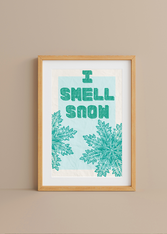 Framed artwork with 'I Smell Snow' text and snowflake designs on a beige wall.