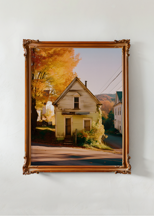 Framed photograph of a house with autumn trees on a white wall